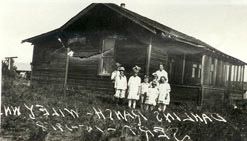 Several people standing in front of the Dahlin home, a plain wooden house in an open field