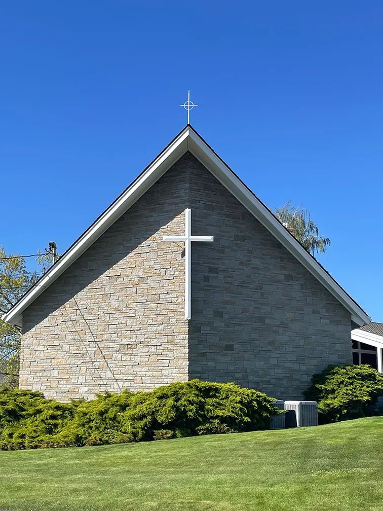The stone front of the church with a white cross under a clear blue sky.