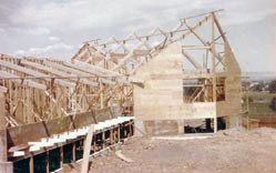 The wooden frame and roof trusses of the new church going up, with the hillside in the distance