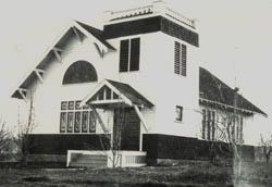 The first church at its dedication, a small white building with a covered entry and a cupola on the roof