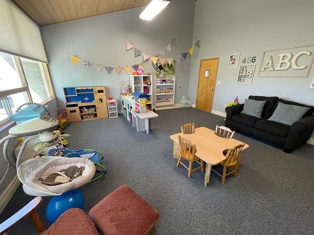 The church nursery, a bright room with a play kitchen, toy shelves, a small table with wooden chairs, and a couch.