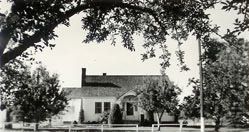 The original church parsonage, a one-story house seen through the branches of orchard trees
